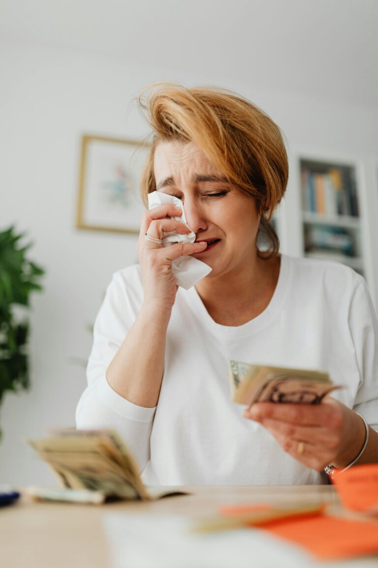 A woman with short hair cries while holding money indoors, showing financial stress.